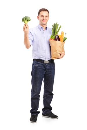 Full length portrait of a young man holding a shopping bag with products and a broccoli in his hand isolated on white backgroundの写真素材