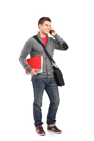 Full length portrait of a smiling school boy holding books and talking on a phone isolated on white backgroundの写真素材