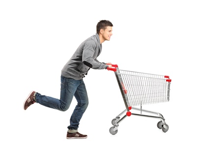 Young man running and pushing an empty shopping cart isolated on white backgroundの写真素材