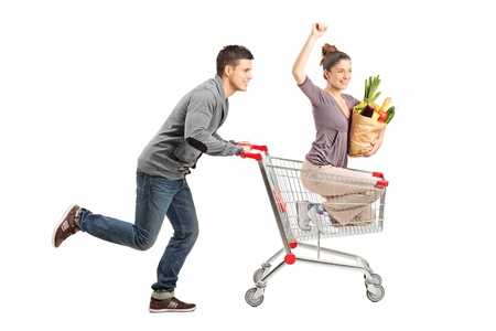 Person pushing a happy woman in a shopping cart with paper bag ful with food isolated on white backgroundの写真素材