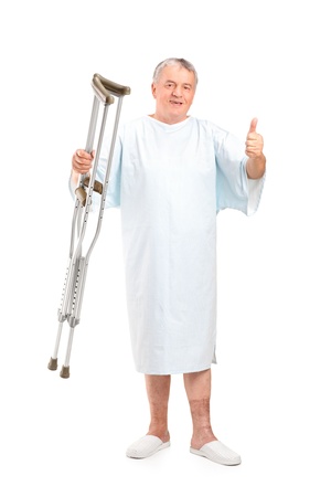 Full length portrait of a senior patient holding crutches and giving thumb up isolated on white backgroundの写真素材