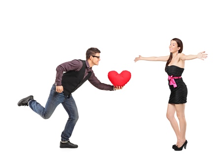 Boyfriend running with a red heart shaped pillow in his hand and an excited girlfriend extending her arms isolated on white backgroundの写真素材