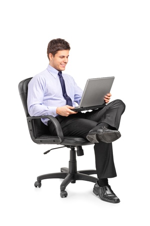 Young smiling businessman sitting in office chair and working on laptop computer isolated on white backgroundの写真素材