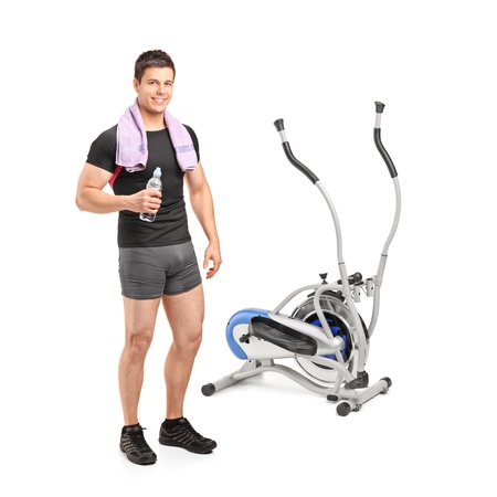 Full length portrait of an athlete standing near a cross trainer machine isolated on white backgroundの写真素材