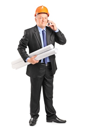 Full length portrait of a mature construction worker holding blueprints and talking on a phone isolated on white background の写真素材