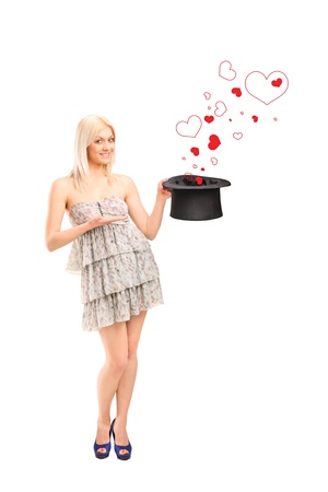 Full length portrait of a smiling woman holding a top hat and hearts coming out isolated on white backgroundの写真素材