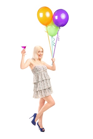 Full length portrait of an attractive woman holding balloons and cocktail isolated on white backgroundの写真素材