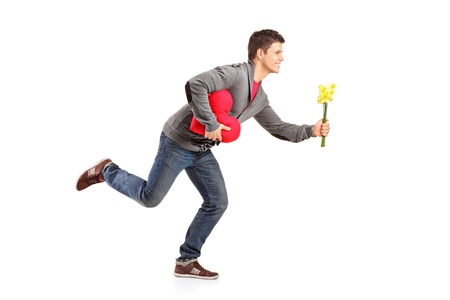 Young man running with a bunch of flowers and red heart shape object in his hands isolated on white backgroundの写真素材
