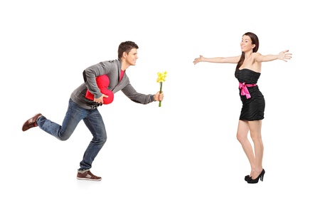 Young man running with a bunch of flowers and red heart shape object and excited female isolated on white backgroundの写真素材
