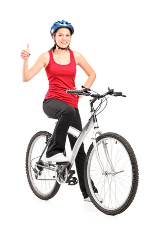 Full length portrait of a female bicyclist posing on a bicycle and giving a thumb up isolated against white backgroundの写真素材