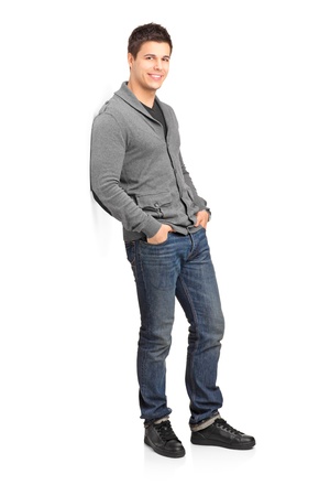 Full length portrait of a smiling male leaning against wall isolated on white backgroundの写真素材