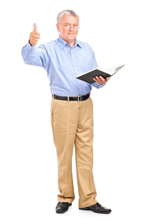 Full length portrait of a male teacher holding a book and giving a thumb up isolated on white backgroundの写真素材