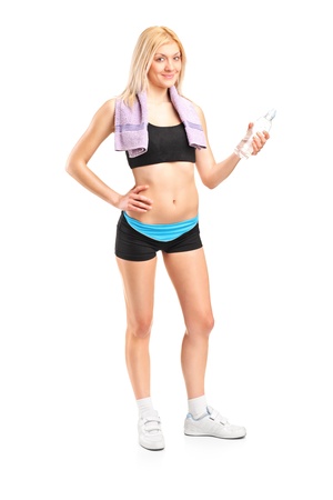 Full length portrait of an attractive sportswoman with a bottle of mineral water posing after a training isolated on white backgroundの写真素材
