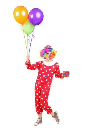 Full length portrait of a male clown, happy joyful expression on face, with a bunch of balloons and a gift isolated on white backgroundの写真素材