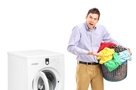 Young man holding a laundry basket and gesturing near a washing machine isolated on white backgroundの写真素材