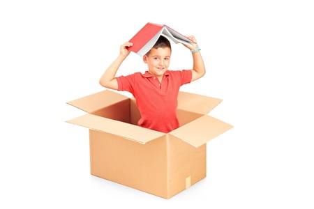 A child in a cardbox holding a book over his head isolated on white backgroundの写真素材