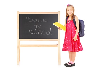 Full length portrait of a schoolgirl holding a notebook and posing next to a board isolated on white backgroundの写真素材