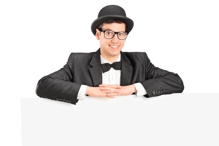 A young male with retro hat and bow tie posing behind a blank panel isolated on white backgroundの写真素材