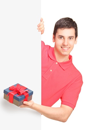 Young handsome man holding a present and standing behind white panelの写真素材