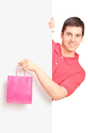 Young male holding a pink bag and standing behind white panelの写真素材