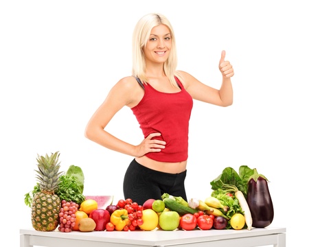 Healthy smiling woman with fruits and vegetables giving a thumb up isolated on white backgroundの写真素材