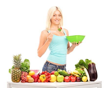 Young woman eating a salad, standing behind table full of fruits and vegetablesの写真素材