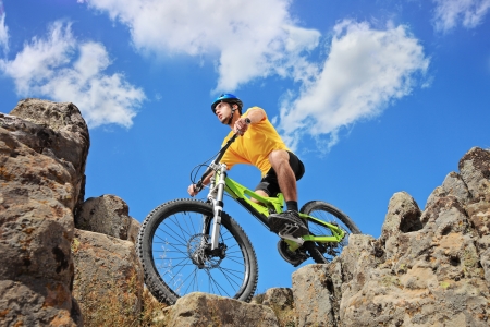 Person riding a mountain bike amid rocks on a sunny day against a blue sky and clouds, low angle viewの写真素材