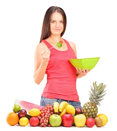 Young woman eating a salad standing behind a pile of fruits isolated on whiteの写真素材