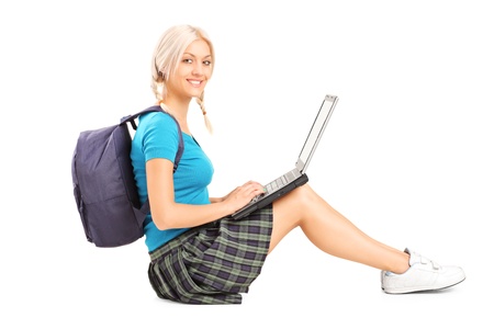 Beautiful blond student working on a laptop and sitting on a floor, isolated on white backgroundの写真素材