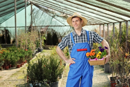 Young worker holding a basket full of flower pots and posing in a gardenの写真素材