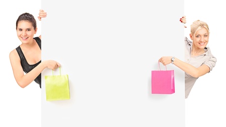 Two females holding a shopping bags and posing behind a white panelの写真素材