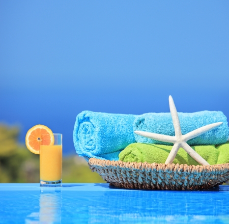 Orange juice, starfish and rolled up towels next to a swimming poolの写真素材