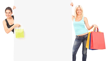 Two females holding a shopping bags behind a white panelの写真素材