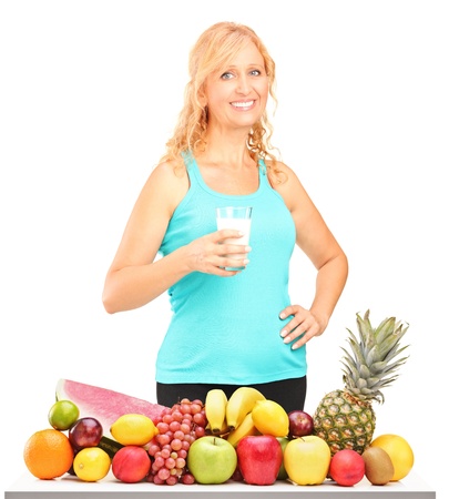Woman holding a glass of milk with pile of fruits on a table, isolated on white backgroundの写真素材