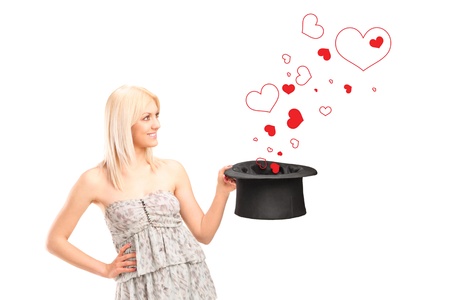 A smiling blond female holding a top hat and hearts around isolated on white backgroundの写真素材