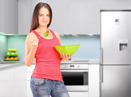 A female eating salad during a breakfast, with kitchen in the backgroundの写真素材