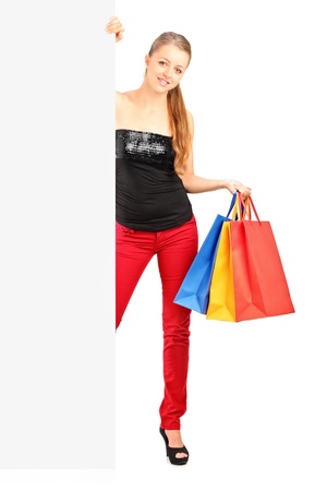Full length portrait of a smiling woman holding a shopping bags behind a white panelの写真素材