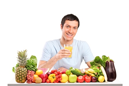 Handsome guy with glass of orange juice, on a table full of fruits and vegetables isolated on white backgroundの写真素材