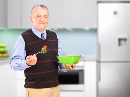 A mature man eating salad during a lunch, with kitchen in the backgroundの写真素材