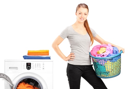 A smiling woman holding a laundry basket next to a washing machine isolated on white backgroundの写真素材
