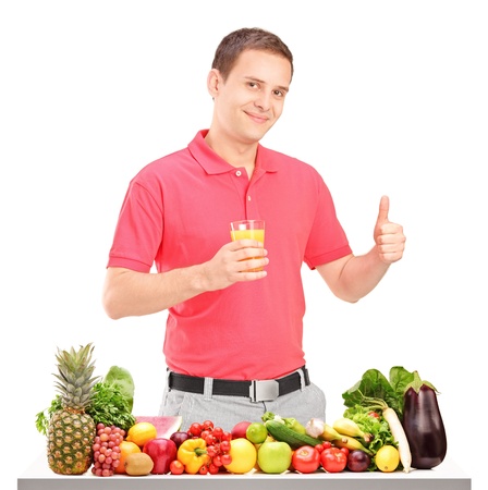 Casual guy holding a juice and giving thumb up with pile of food on a table, isolated on white backgroundの写真素材
