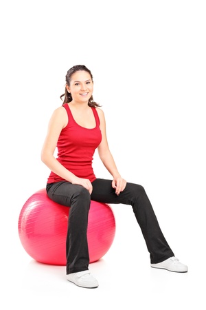 Portrait of a young female sitting on a pilates ball isolated on white backgroundの写真素材