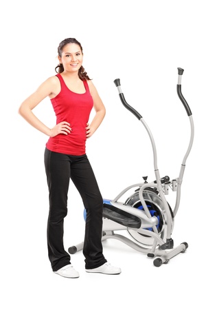 Young female posing next to a cross trainer isolated on white backgroundの写真素材