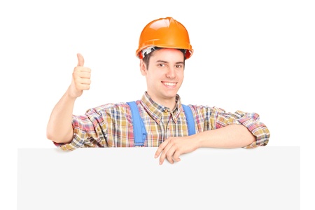 A happy male construction worker posing behind a blank panel giving thumb upの写真素材