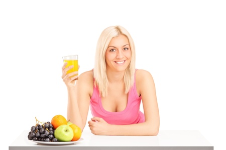 Blond smiling female holding a glass of orange juice on a table isolated on white backgroundの写真素材