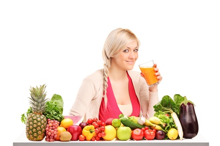 Beautiful woman drinking orange juice, on a table full of fruits and vegetables isolated on white backgroundの写真素材