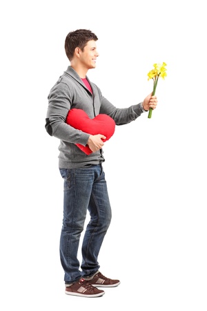 Full length portrait of a young man holding a heart shaped object and flowers isolated on white backgroundの写真素材