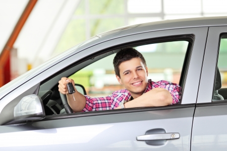 A smiling male sitting in his automobile and holding a car keyの写真素材