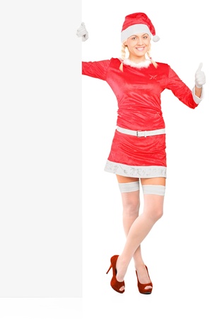 Beautiful and sexy female wearing santa claus costume holding a panel and giving a thumb up isolated on whiteの写真素材