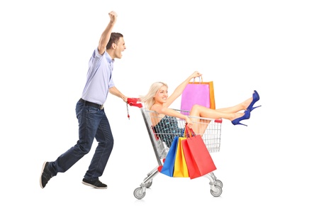 Excited person pushing a shopping cart, happy woman with bags in it, isolated on white backgroundの写真素材